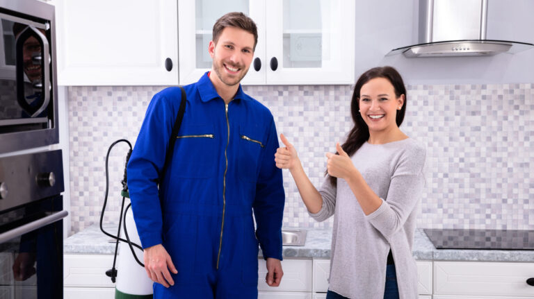 a man and a woman posing for a photo indoors, likely in a kitchen. They are both smiling and standing.