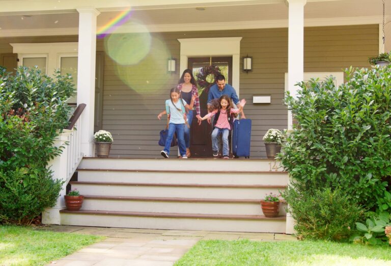 A family exits on the steps of a house carrying bags.