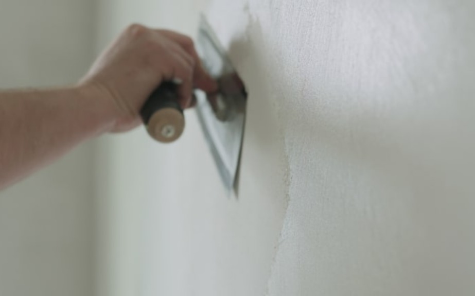 A person indoors holding a clipboard. There is a wall in the background and he is plastering it.